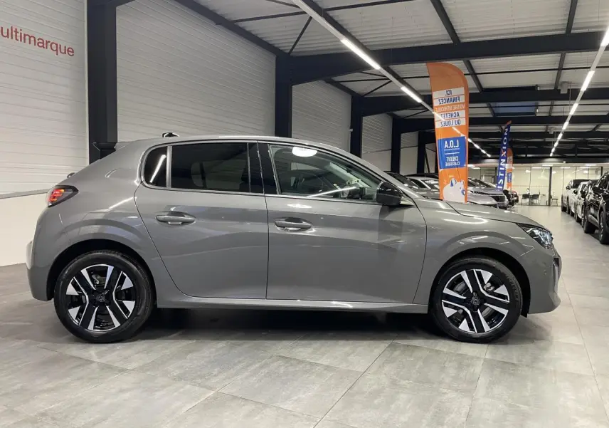 Profil côté gauche d'une Peugeot 208 gris sélénium 2025 avec jantes alliage bi-ton dans un showroom.