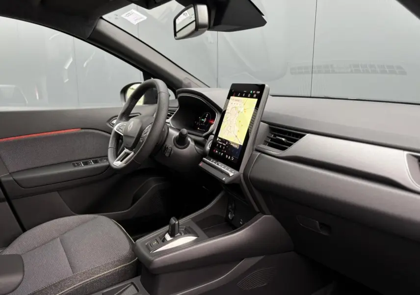 Vue intérieure côté conducteur du Renault Captur 2025, tableau de bord noir avec écran tactile vertical et volant multifonction.