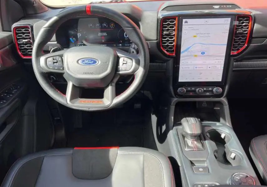 Vue intérieure avant du Ford Ranger Raptor 2025, volant cuir noir avec surpiqûres rouges et écran tactile vertical.