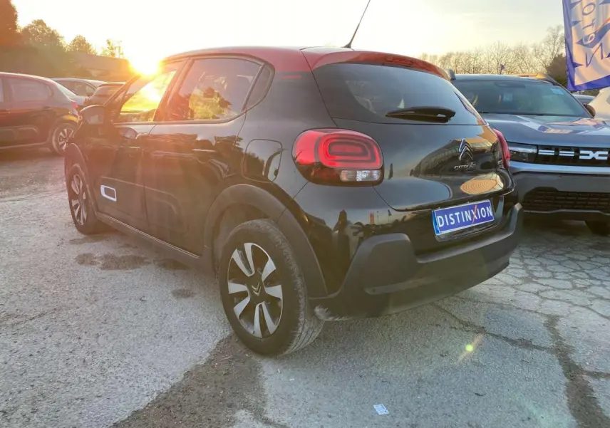 Vue 3/4 arrière gauche d'une Citroën C3 noire avec toit rouge, jantes diamantées et feux arrière LED au soleil couchant.