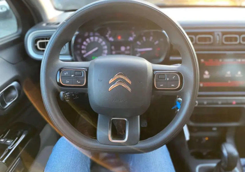 Vue intérieure centrée sur le volant Citroën C3 Shine 2023 avec commandes audio et tableau de bord éclairé.