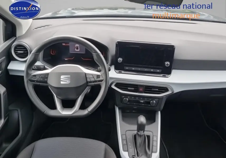 Vue intérieure du poste de conduite de la SEAT Arona 2025, volant cuir méplat et tableau de bord gris clair.