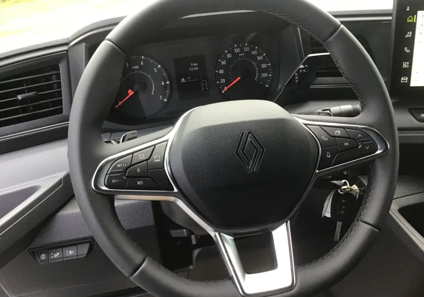 Vue rapprochée du volant noir du Renault Master 2025, avec commandes intégrées et tableau de bord digital en arrière-plan.