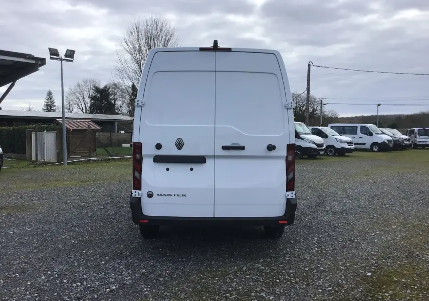 Vue arrière d’un utilitaire Renault Master blanc stationné sur un sol gravillonné avec plusieurs autres véhicules en arrière-plan.