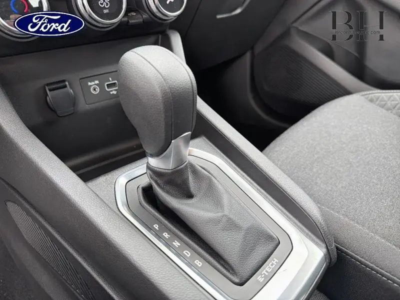 Gros plan sur la console centrale noire avec levier de vitesse automatique et surpiqûres tissu gris du siège passager.
