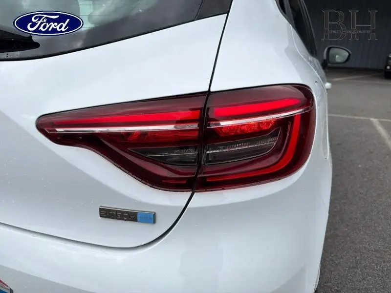 Gros plan sur le feu arrière droit d'une Renault Clio blanche 1.6 E-Tech hybride avec badge hybride bleu.