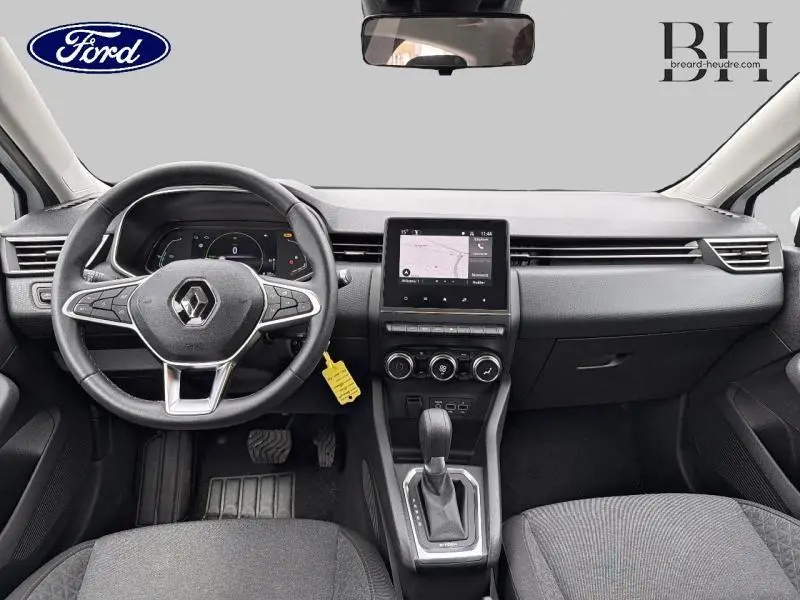 Vue intérieure avant du tableau de bord et volant noir d'une Renault Clio blanche hybride avec écran tactile central et boîte automatique.