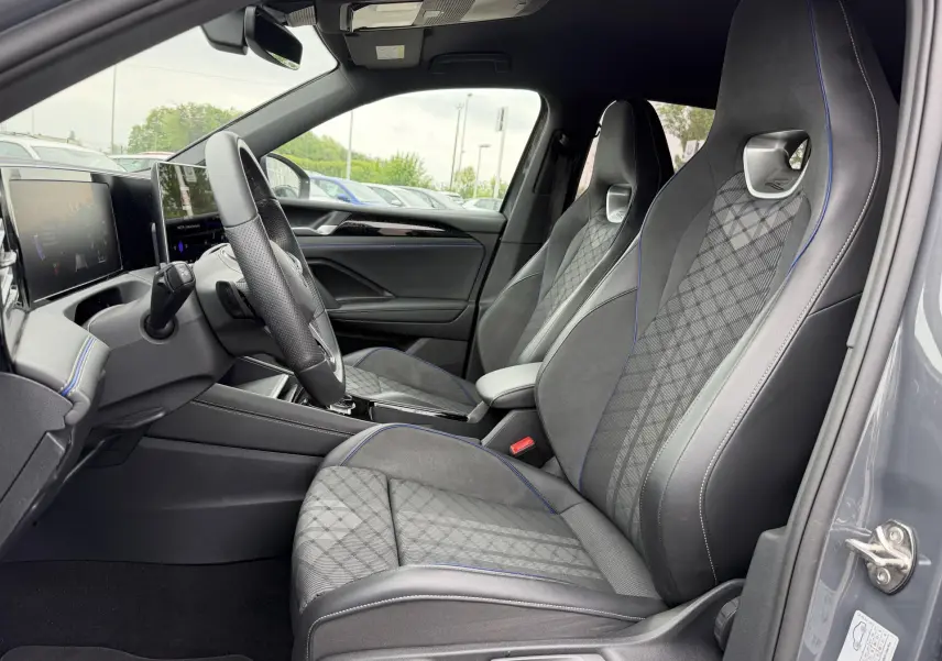 Vue intérieure côté conducteur du Volkswagen Tiguan gris 2025, sièges sport en tissu et cuir avec surpiqûres bleues.
