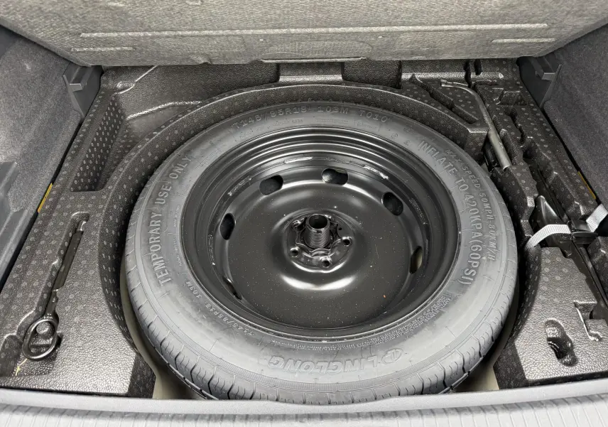 Vue plongeante sur la roue de secours compacte noire dans le coffre du Volkswagen Tiguan gris 2025.