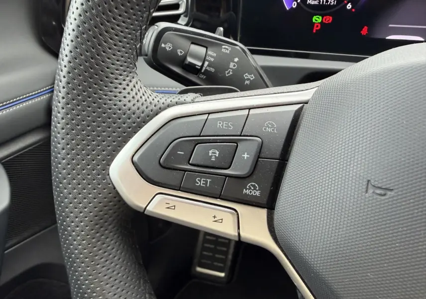 Gros plan sur le volant cuir perforé du Volkswagen Tiguan 2025 avec commandes de régulateur de vitesse et tableau de bord numérique.