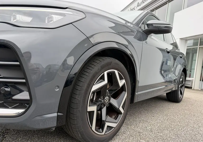 Vue de profil avant droit du Volkswagen Tiguan gris métallisé, mettant en valeur la jante alliage 19 pouces et les projecteurs LED.