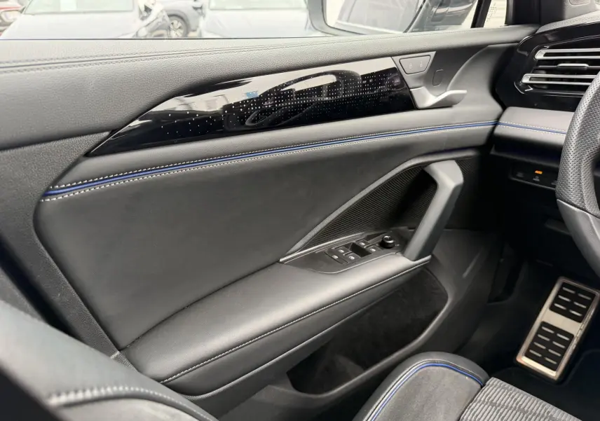 Détail de la porte avant gauche du Volkswagen Tiguan 2025, intérieur noir avec surpiqûres bleues et inserts brillants.