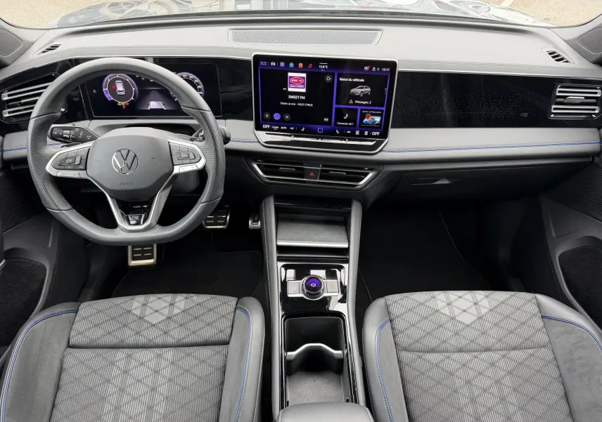 Vue intérieure avant du Volkswagen Tiguan 2025, tableau de bord noir avec écran tactile central et volant multifonction cuir.