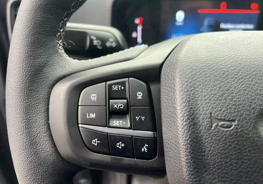Gros plan sur les commandes multifonctions à gauche du volant cuir du Ford Ranger gris carbone 2025.