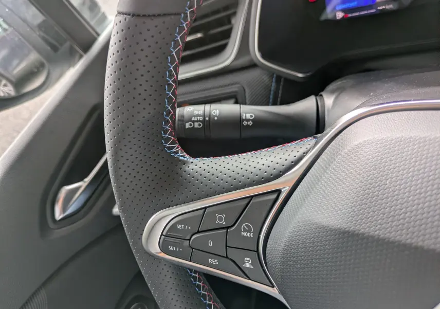 Gros plan sur le volant perforé avec surpiqûres tricolores du Renault Symbioz, montrant les commandes intégrées côté gauche.