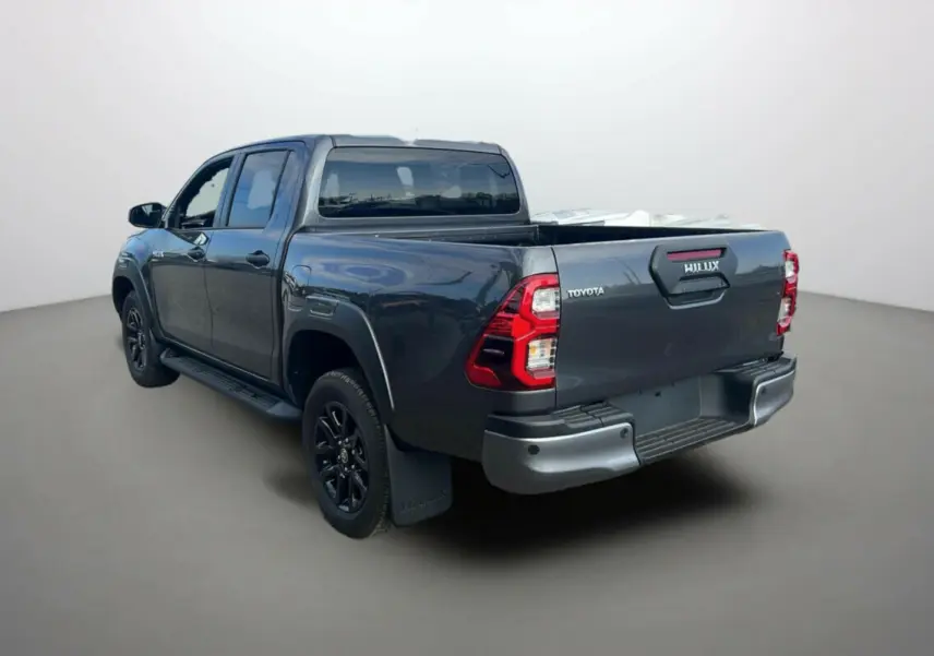 Toyota Hilux 4x4 gris atlas vue 3/4 arrière droit, avec benne ouverte et jantes noires distinctives.