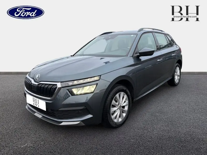 Vue 3/4 avant d'une Skoda Kamiq 1.0 TSI Business gris météore avec calandre chromée et phares LED allumés.