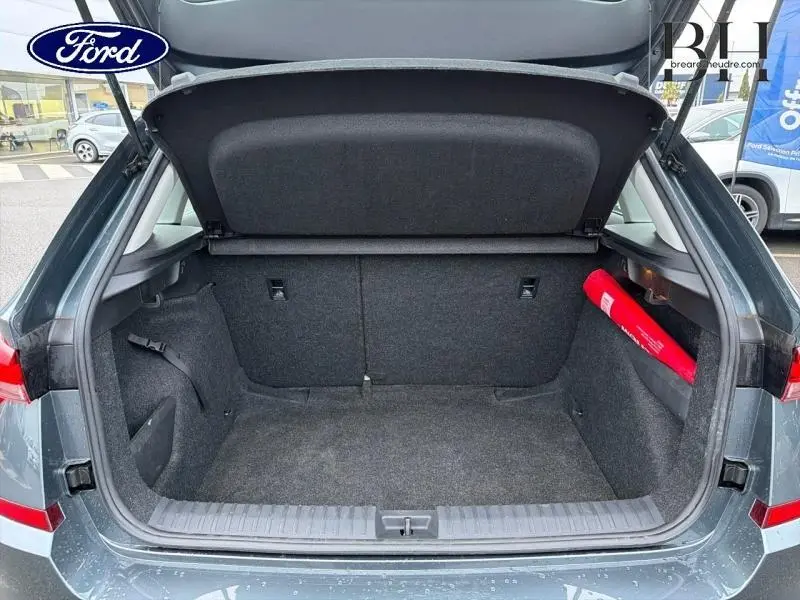 Coffre ouvert vu de l'arrière d'une Skoda Kamiq gris météore avec tapis et triangle de sécurité rouge visible à droite