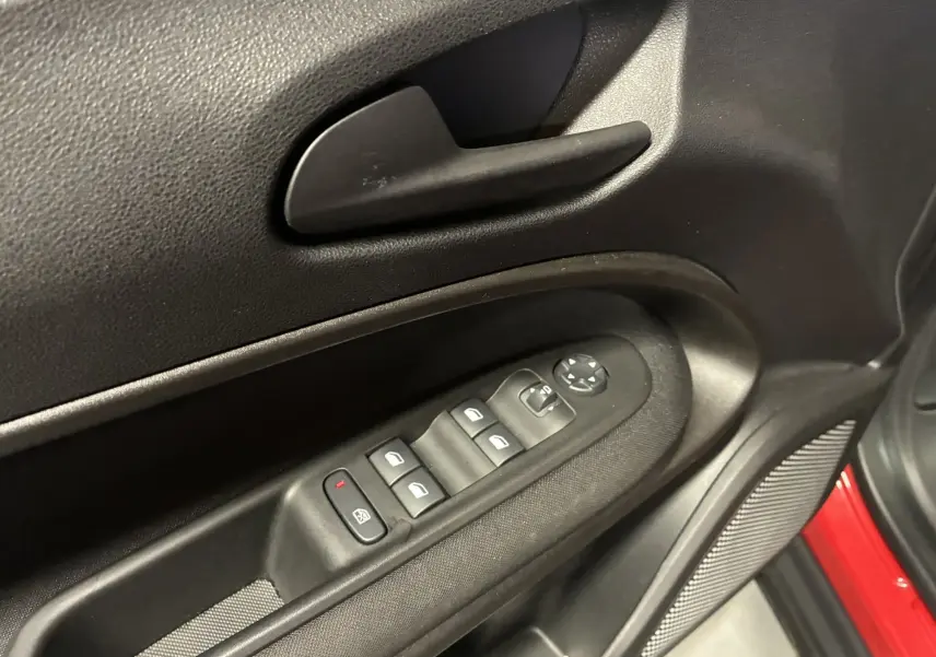 Détail de la porte côté conducteur avec commandes électriques et poignée noire, intérieur tissu noir, bord rouge visible.