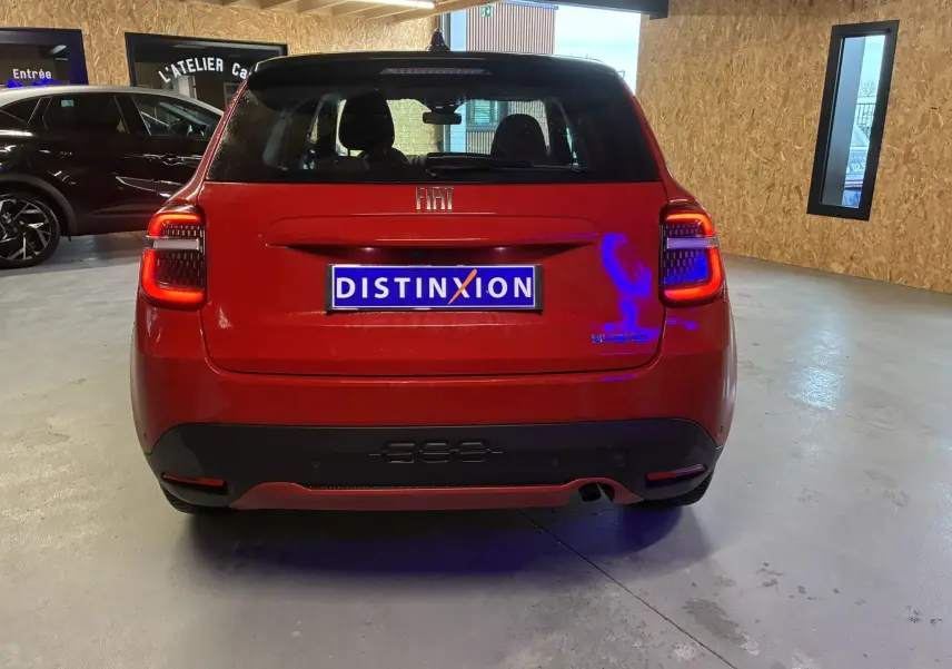 Vue arrière d'une FIAT 600 rouge 2024 hybride, avec feux arrière allumés et logo distinctif sur le hayon.