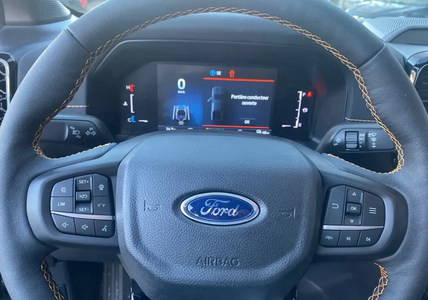 Vue rapprochée du volant en cuir noir avec surpiqûres orange du Ford Ranger 2025, affichage digital au tableau de bord.