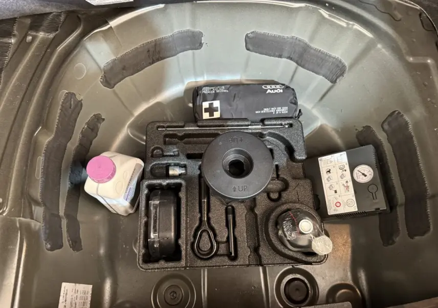 Vue plongeante sur le coffre noir d’une Audi A1 2021, montrant le rangement pour roue de secours et accessoires.