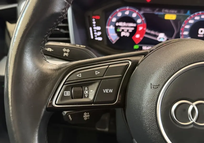 Gros plan sur le volant cuir noir multifonctions d'un Audi A1 2021 avec affichage numérique en arrière-plan.