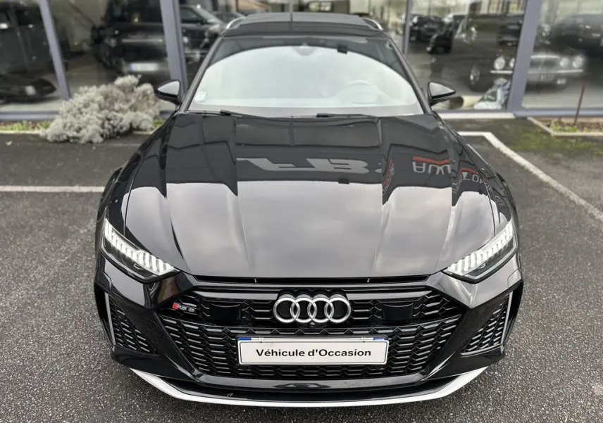 Vue avant d'une Audi RS6 Avant noire 2021 avec calandre noire et phares LED allumés sur parking.