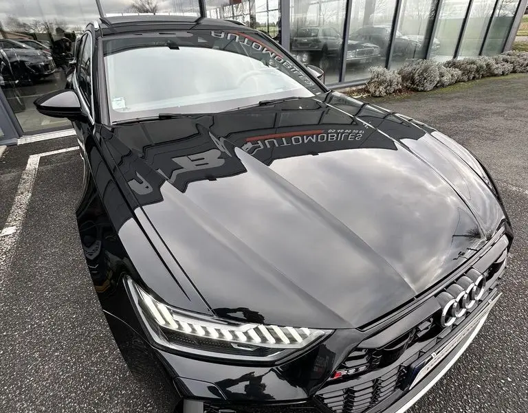 Audi RS6 Avant noir vue 3/4 avant droit, phares LED allumés et calandre sport avec logo RS6 visible.