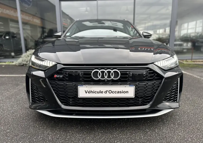 Vue frontale d'une Audi RS6 Avant noire 2021 avec calandre hexagonale et phares LED allumés.
