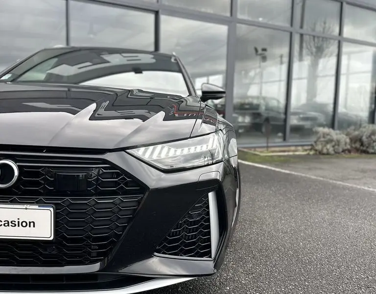 Vue de face rapprochée d'une Audi RS6 Avant noire 2021 avec calandre hexagonale et phares LED allumés.