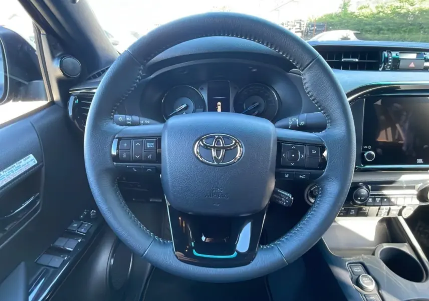 Vue intérieure centrée sur le volant en cuir noir du Toyota Hilux 4x4 2025 avec tableau de bord et commandes visibles.
