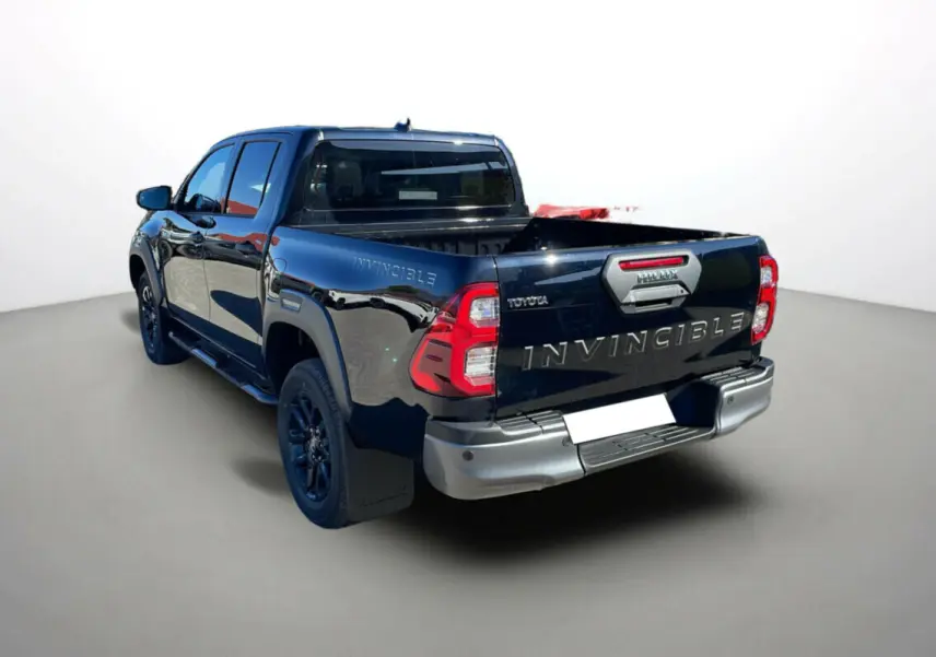 Toyota Hilux 4x4 Invincible 2025 en noir attitude, vue arrière 3/4 gauche avec benne ouverte et jantes noires.