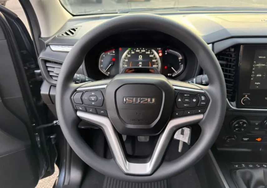 Vue rapprochée du volant multifonctions noir de l'Isuzu D-MAX 2026 avec tableau de bord et écran tactile visibles.