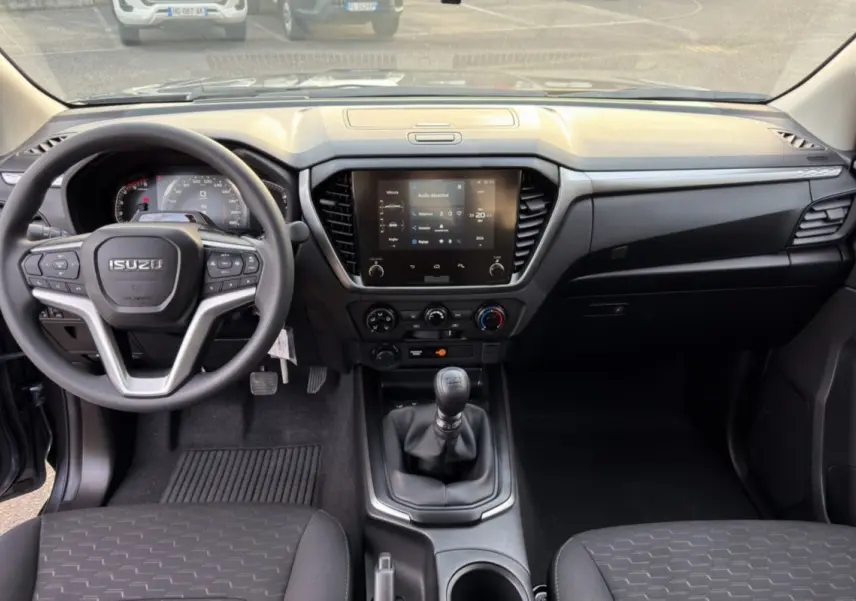 Vue intérieure avant de l'Isuzu D-MAX 2026 avec tableau de bord noir et écran tactile central allumé.