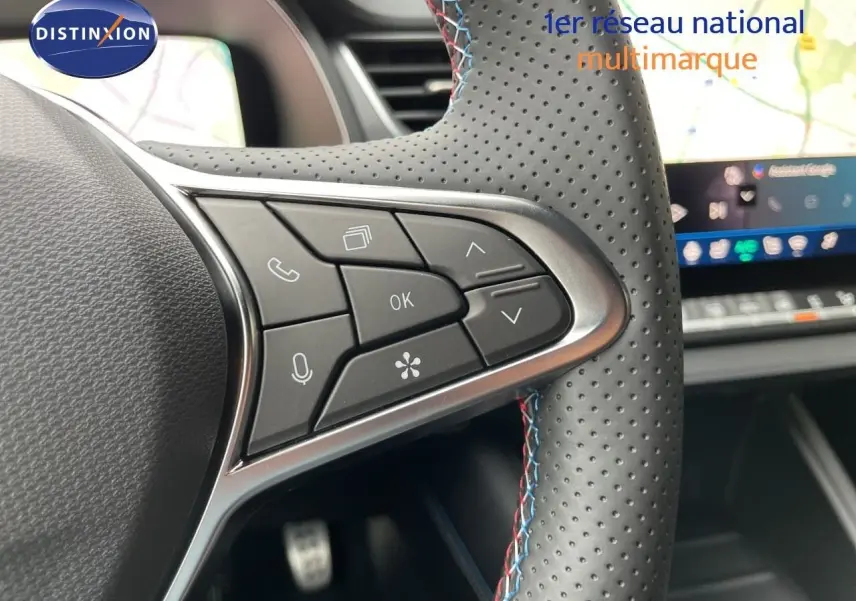 Gros plan sur les commandes du volant perforé avec surpiqûres tricolores du Renault Symbioz gris Rafale, tableau de bord numérique en arrière-plan.