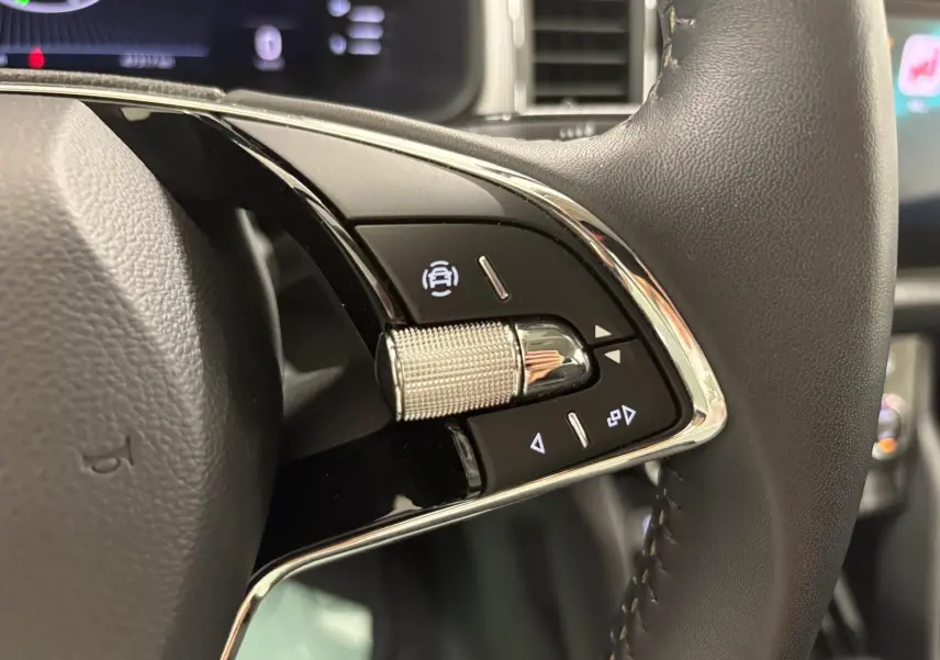 Gros plan sur les commandes du volant du Skoda Kodiaq blanc Lune, soulignant le bouton de régulateur de vitesse.