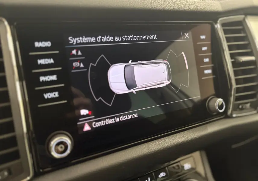 Écran central du Skoda Kodiaq blanc lune montrant le système d'aide au stationnement en vue du dessus.