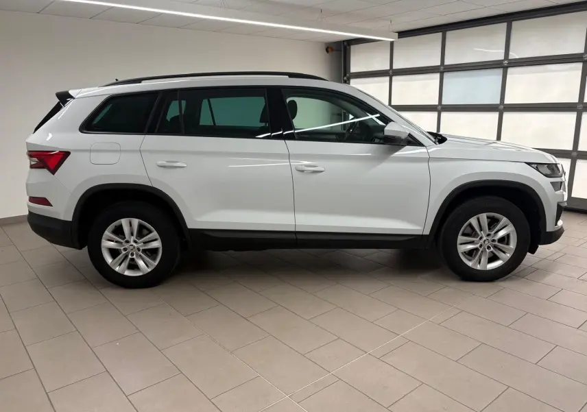 Vue de profil côté gauche d'un Skoda Kodiaq blanc Lune 2022 en intérieur, avec jantes alliage et attelage escamotable.