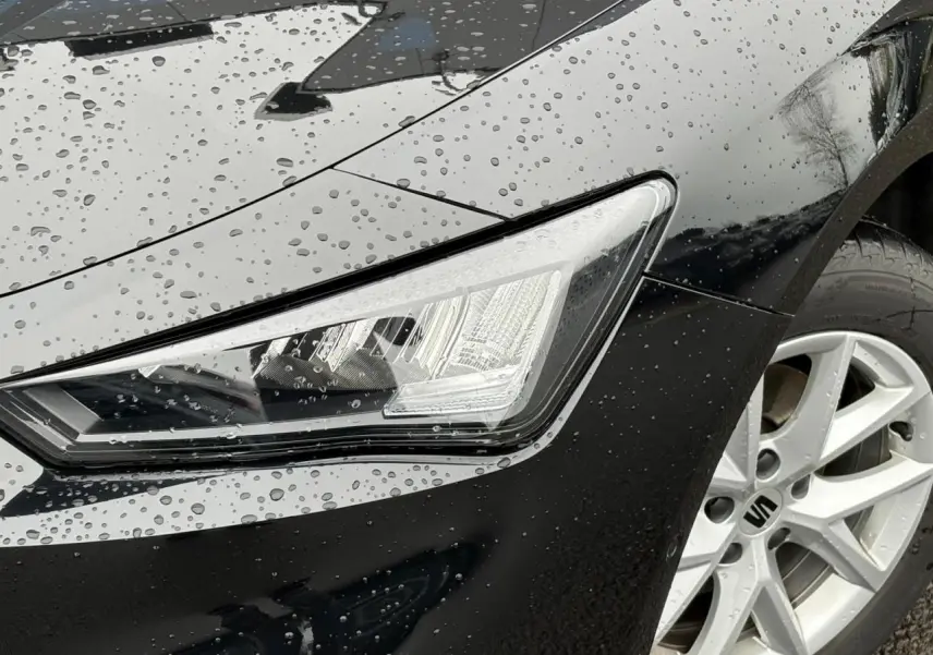 Gros plan sur le phare avant droit et la jante alliage 16 pouces d'une SEAT LEON 2.0 TDI noir Minuit sous la pluie.