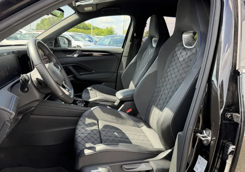 Intérieur avant du Volkswagen Tiguan noir 2025, vue côté conducteur, sièges sport avec surpiqûres bleues et volant cuir multifonction.