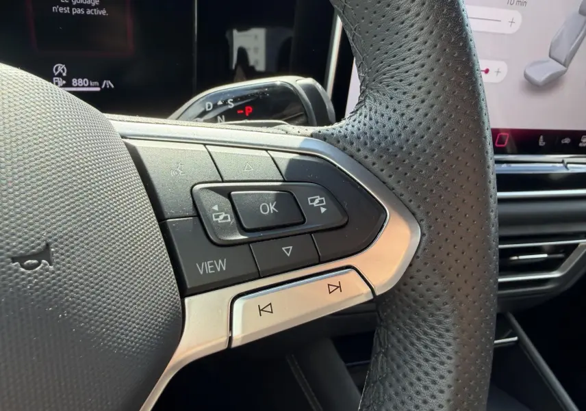 Gros plan sur le côté gauche du volant cuir perforé du Volkswagen Tiguan 2025 avec commandes multifonctions et écran digital en arrière-plan.