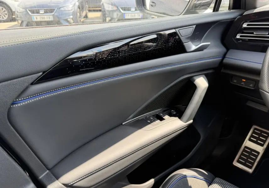 Détail de la porte avant gauche noire du Volkswagen Tiguan 2025 avec surpiqûres bleues et commandes électriques.