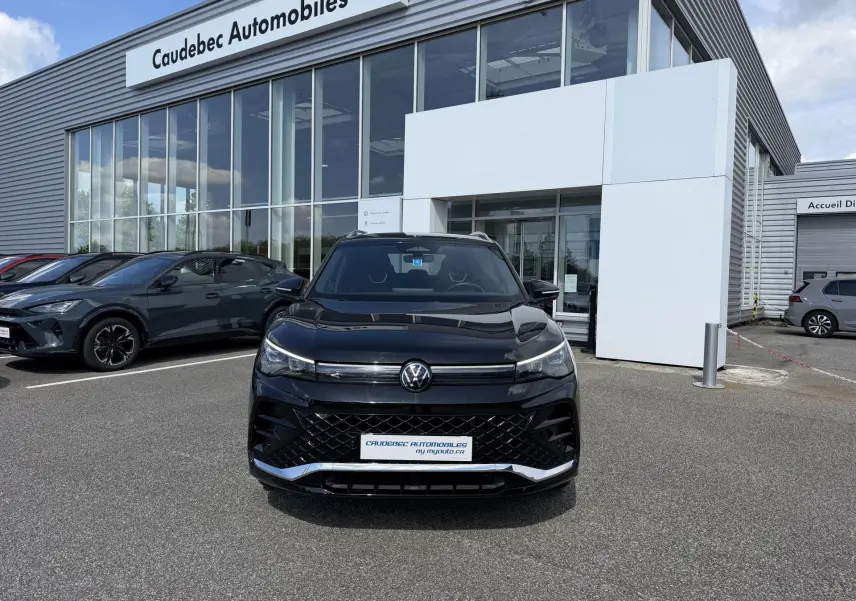 Vue avant d'un Volkswagen Tiguan noir 2025 avec calandre noire et détails chromés, stationné devant un concessionnaire.