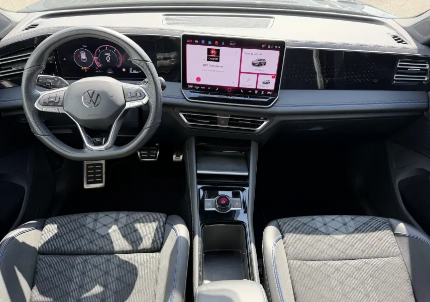 Vue intérieure avant du Volkswagen Tiguan 2025 avec tableau de bord digital, volant sport et sellerie tissu noire à surpiqûres bleues.