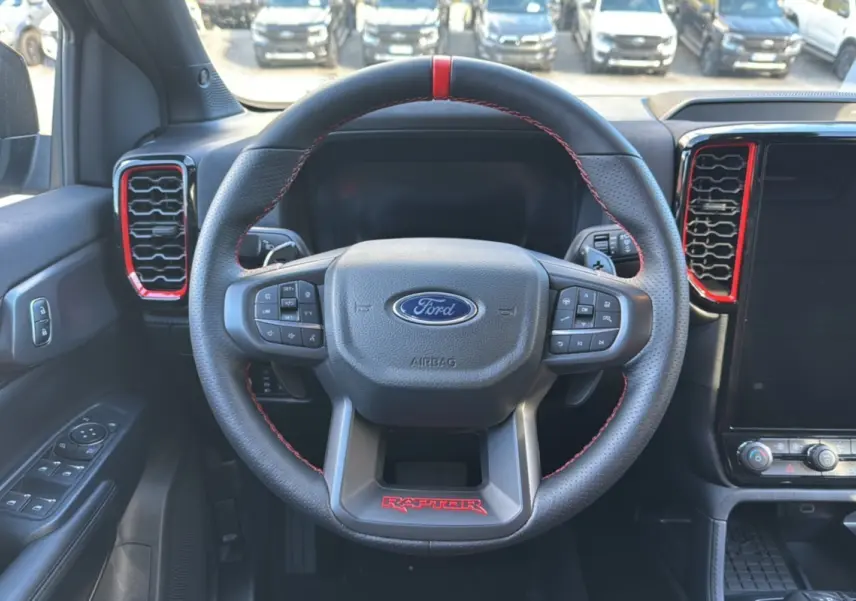 Vue intérieure centrée sur le volant noir du Ford Ranger Raptor 2024 avec surpiqûres rouges et détails rouges autour des aérateurs.