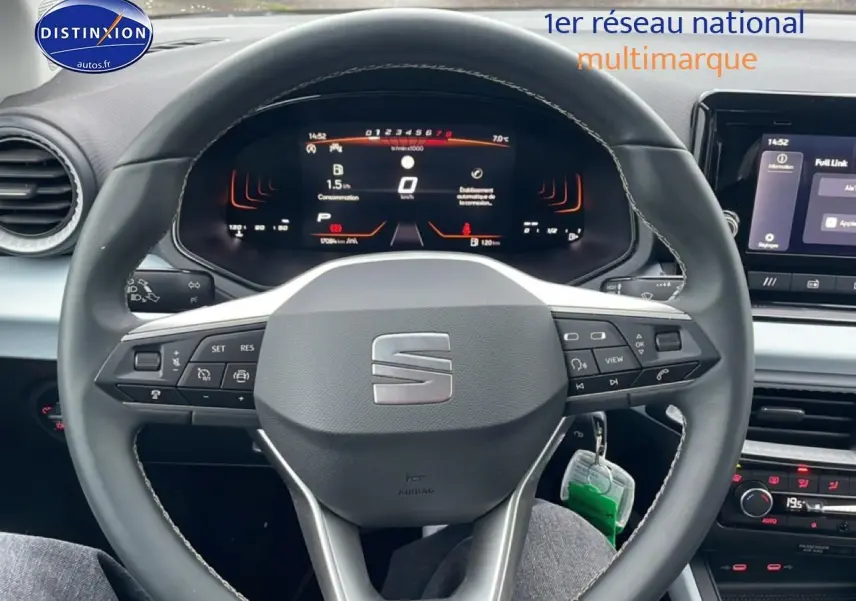 Vue intérieure centrée sur le volant cuir noir avec logo SEAT, tableau de bord digital et écran tactile du SEAT Arona blanc Nevada.