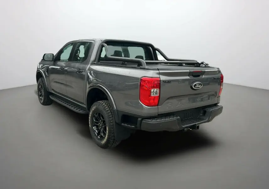 Vue 3/4 arrière droite du Ford Ranger gris carbone avec arceaux noirs et attelage visible sur fond neutre.