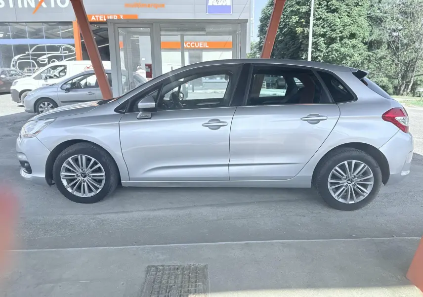 Profil côté gauche d'une Citroën C4 gris clair 5 portes, garée sous un abri avec jantes alliage visibles.
