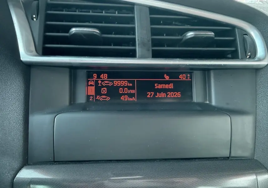 Affichage central du tableau de bord de la Citroën C4 gris, montrant l'horloge, la date et les informations de conduite.